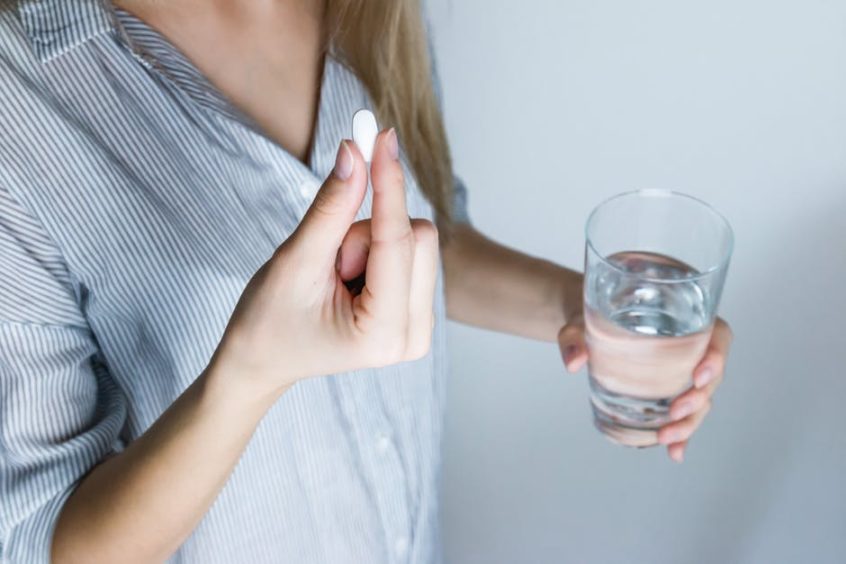 woman holding a pill in one hand and water in the other